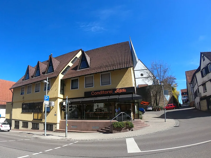 Die Conditorei Schütz an der Straßenecke neben der Benninger Kirche bei blauem Himmel